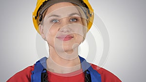 Young woman in yellow hardhat walking on gradient background.