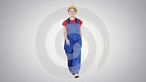 Young woman in yellow hardhat walking on gradient background.