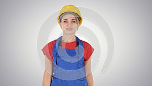 Young woman in yellow hardhat walking on gradient background.