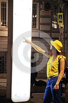 Young woman in a yellow hat looks at the electronic map of the city. Moscow night and tourism concept