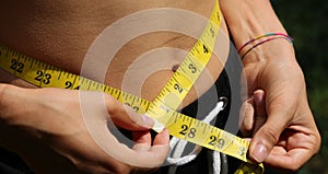 young woman with yellow meter while measuring waistline and numbers in inches