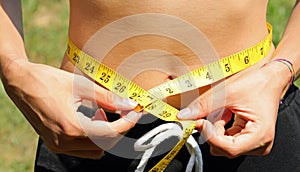 young woman and yellow meter while measuring waistline and numbers in inches