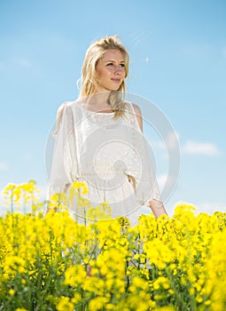 Young woman in yellow oilseed rape field posing in white dress