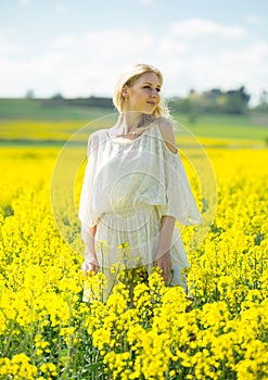 Young woman in yellow oilseed rape field posing in white dress