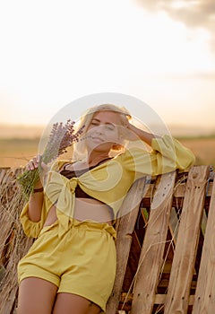 Young woman in yellow among rural field with golden oat field on sunset background