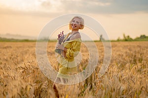 Young woman in yellow among rural field with golden oat field on sunset background