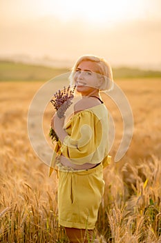 Young woman in yellow among rural field with golden oat field on sunset background