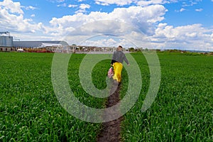 A young woman in a yellow skirt and a leather jacket walks with a backpack along the path in the field