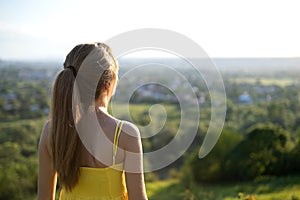 Young woman in yellow summer dress standing in green meadow enjoying sunset view