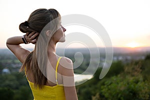 Young woman in yellow summer dress standing in green meadow enjoying sunset view