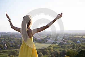 Young woman in yellow summer dress standing in green meadow enjoying sunset view