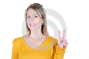 Young woman with yellow sweater over isolated white background smiling showing victory finger sign