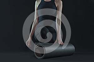 Young woman with yoga mat practicing yoga on dark black background. front view