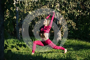 Young womanin red sportswear doing yoga warrior pose in the autumn park