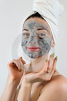 Young womanin white towel applying mud black mask on her face isolated on white, spa treatment