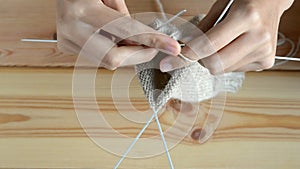Young womans hands knitting with gray metal needles and woolen thread on wooden table background