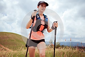 Young women active trail running across a meadow on a grassy trail high in the mountains in the afternoon with trekking pole