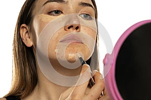Young women applying concealer under her eyes and face