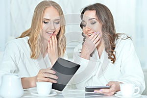 Young women in bathrobes using digital devices