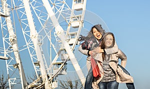 Young women best friends enjoying time together with piggyback at luna park ferris wheel