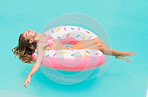 Young women in bikini lying down on an inflatable donut in swimming pool. Girl enjoys sunbathing on floating pool inflatable toy o