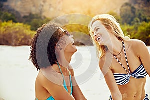 Young women in bikinis laughing together on a sandy beach