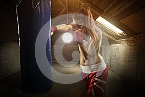 Young women boxing, hitting the boxing bag - on the attic