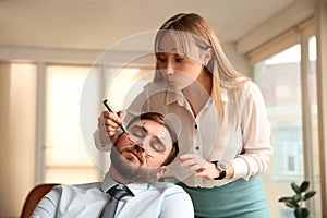 Young woman drawing on colleague`s face while he sleeping in office. Funny joke