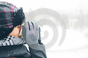 Young women dressed in warm hat coat scarf and gloves outside with paper glass in hands. Snow on her clothes. She drink