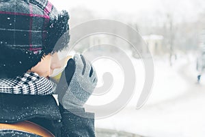 Young women dressed in warm hat coat scarf and gloves outside with paper glass in hands. Snow on her clothes. She wants