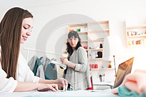 Young women dressmaster create new concept clothing with contemporary laptop in sewing showroom. Seamstress workin