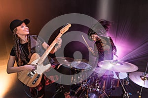 Young women with drums set and electric guitar performing rock concert on stage