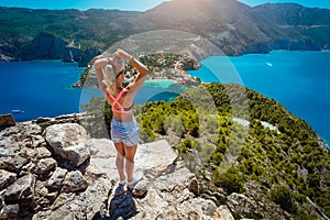 Young women enjoying view to Assos village Kefalonia from top castle. Beautiful blue colored bay lagoon underneath