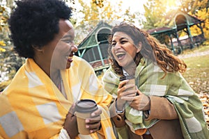 Young women friends chatting outdoors and drinking coffee while enjoying the walk in the park together