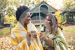 Young women friends chatting outdoors and drinking coffee while enjoying the walk in the park together