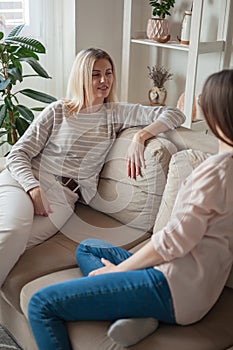 Young women friends talking, smiling together, sitting on sofa a