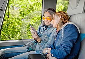 Young women friends travel by bus and using mobile internet on their smartphone during trip