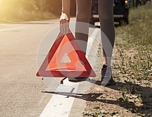 Young women hands close up putting triangle caution sign on road near broken car on roadside