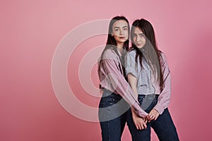 Young women having fun in the studio with pink background. Adorable twins