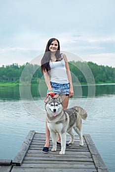 Young women and her dog husky is sitting in a park near lake in summer