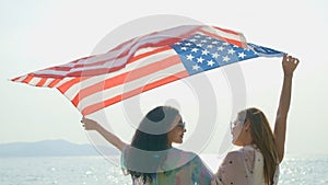 Young women hold American flags on the beach and the sea on their summer vacation and they smile and enjoy their vacation