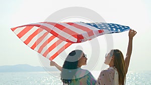 young women hold American flags on the beach and the sea on their summer vacation and they smile and enjoy their vacation