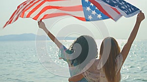 young women hold American flags on the beach and the sea on their summer vacation and they smile and enjoy their vacation
