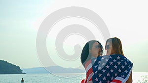 young women hold American flags on the beach and the sea on their summer vacation and they smile and enjoy their vacation