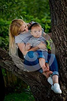 A young woman in jeans and a striped T-shirt and her little daughter are sitting on a tree