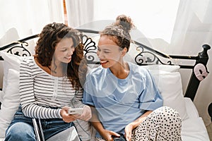 Young women laughing and using cellphones while lying in bed at home