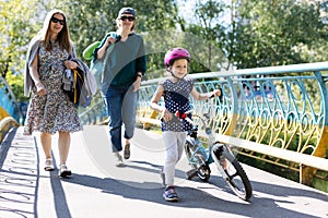 Young women and little girl with bicycle walking in park