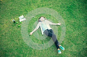 Young women lying in summer grass with headphones listening to music and playing notebook relaxing,