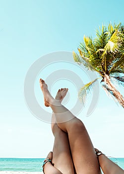 Young women lying on a tropical beach, relax stretching up slender legs tanned