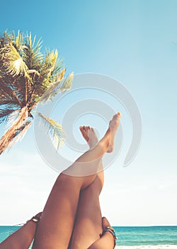 Young women lying on a tropical beach, relax stretching up slender legs tanned.